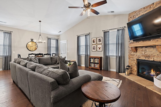 living room featuring ceiling fan with notable chandelier, a stone fireplace, dark wood-style flooring, and visible vents