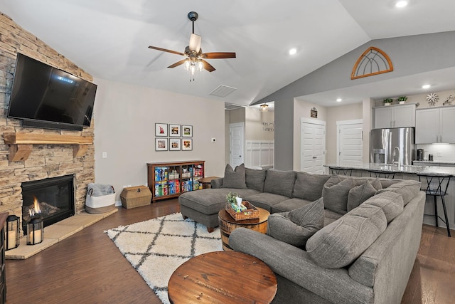 living area with dark wood-style floors, a fireplace, visible vents, vaulted ceiling, and ceiling fan