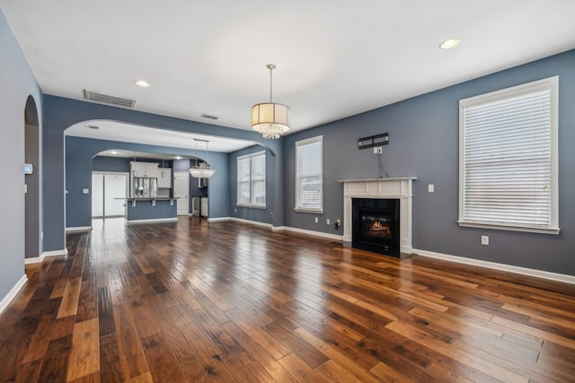 unfurnished living room with a fireplace with flush hearth, visible vents, dark wood finished floors, and baseboards