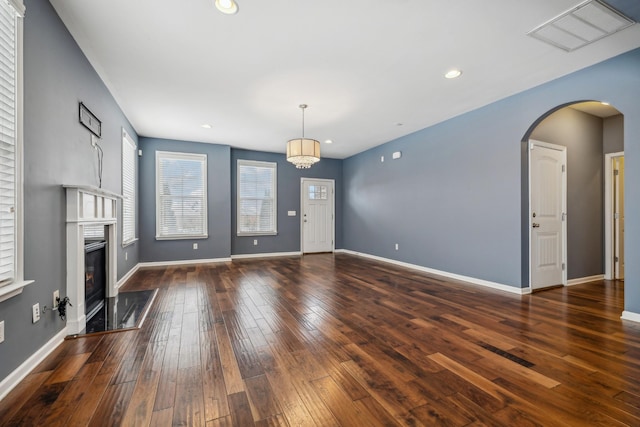 unfurnished living room with arched walkways, dark wood-style flooring, visible vents, baseboards, and a glass covered fireplace