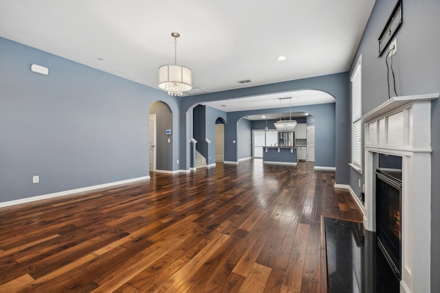 unfurnished living room with dark wood-style floors, a warm lit fireplace, baseboards, and arched walkways