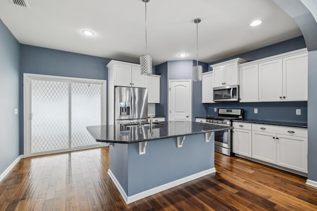 kitchen with hanging light fixtures, appliances with stainless steel finishes, a kitchen island with sink, a sink, and white cabinetry