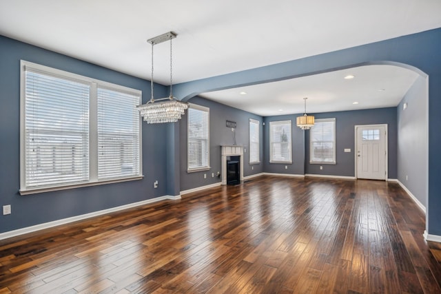 unfurnished living room with dark wood-style floors, arched walkways, a chandelier, and a glass covered fireplace