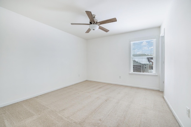 spare room featuring a ceiling fan, light carpet, and baseboards