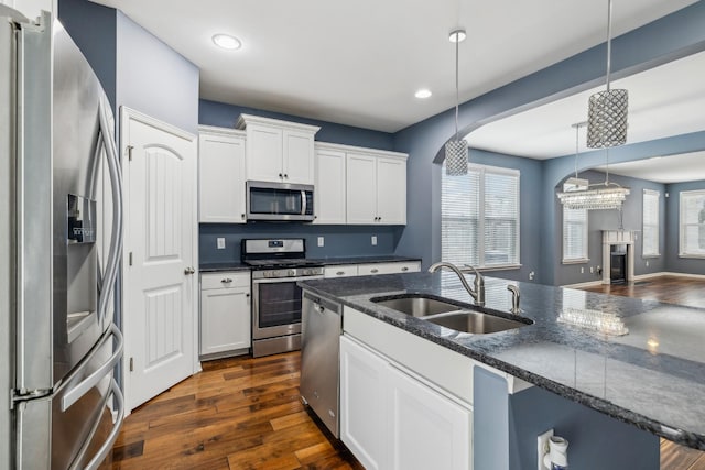 kitchen featuring dark stone counters, hanging light fixtures, stainless steel appliances, white cabinetry, and a sink