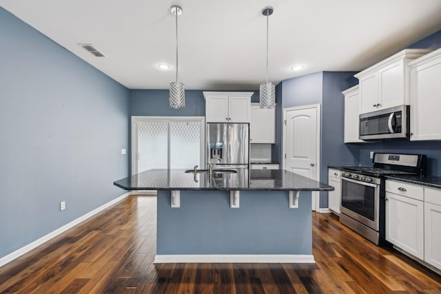 kitchen with pendant lighting, a center island with sink, appliances with stainless steel finishes, white cabinetry, and dark stone counters