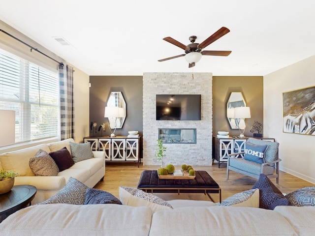 living room with a ceiling fan, a fireplace, visible vents, and wood finished floors