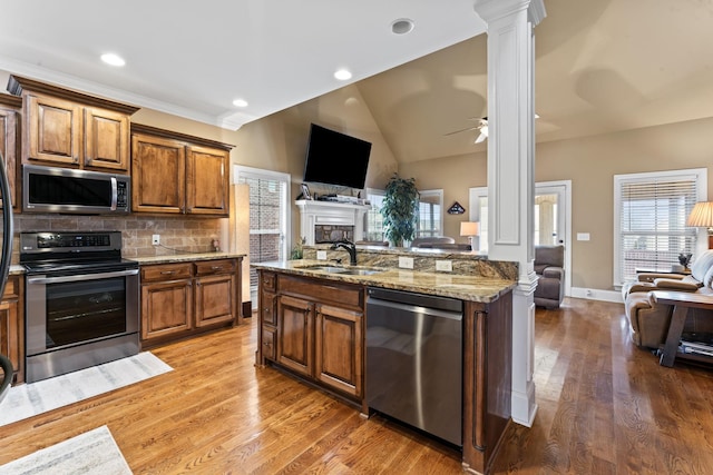 kitchen featuring stainless steel appliances, brown cabinetry, open floor plan, a sink, and ornate columns