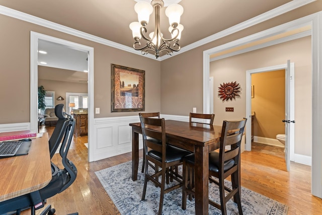 dining space featuring a wainscoted wall, a chandelier, wood finished floors, and ornamental molding