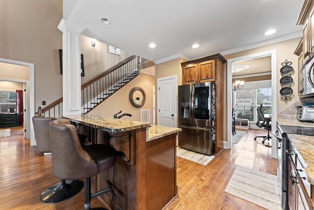 kitchen featuring brown cabinetry, a kitchen island, a breakfast bar area, light stone countertops, and stainless steel appliances