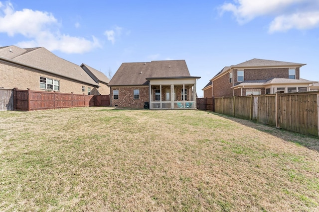 rear view of house with a yard, brick siding, and a fenced backyard