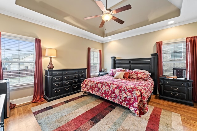 bedroom with a tray ceiling, multiple windows, and light wood-style flooring