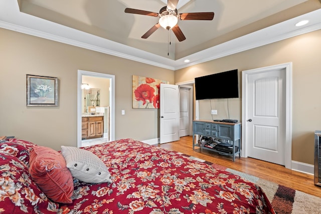 bedroom featuring a raised ceiling, light wood-style flooring, ensuite bathroom, ornamental molding, and baseboards