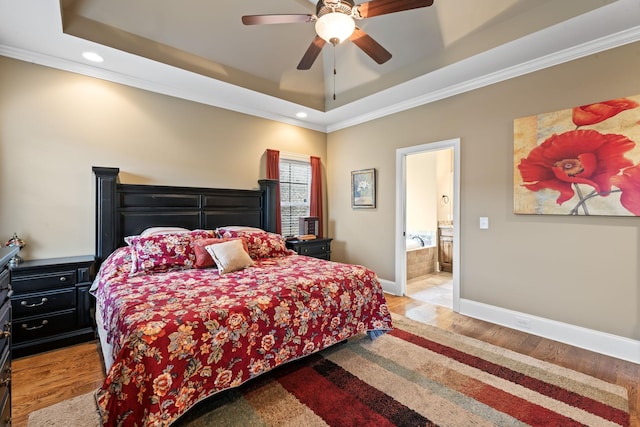 bedroom with ensuite bathroom, baseboards, ornamental molding, a tray ceiling, and light wood finished floors