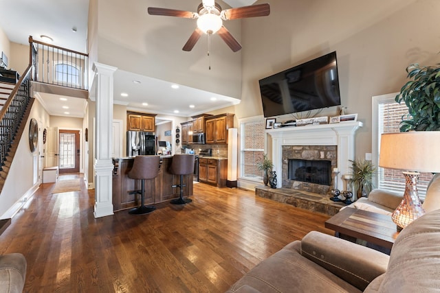 living area with dark wood-style flooring, a fireplace, a towering ceiling, stairway, and ornate columns