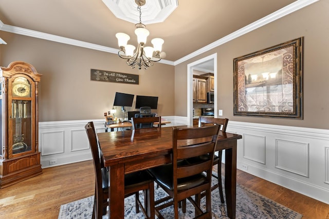 dining area featuring a wainscoted wall, wood finished floors, crown molding, a chandelier, and a decorative wall