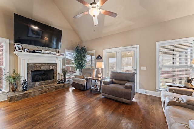 living area featuring baseboards, a ceiling fan, dark wood-type flooring, a stone fireplace, and high vaulted ceiling