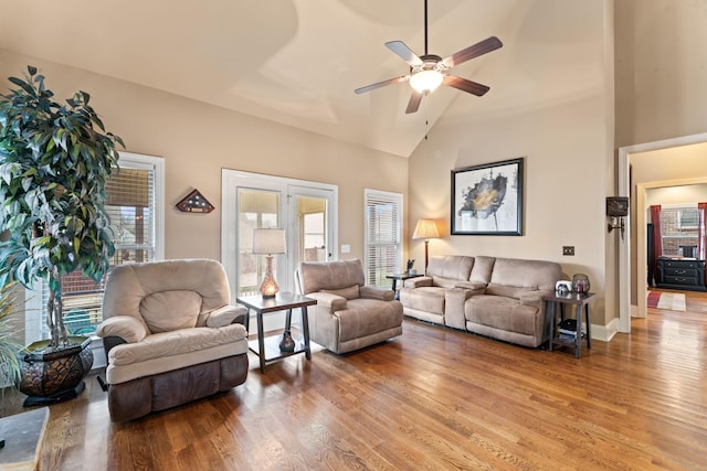 living area with ceiling fan, high vaulted ceiling, wood finished floors, and baseboards