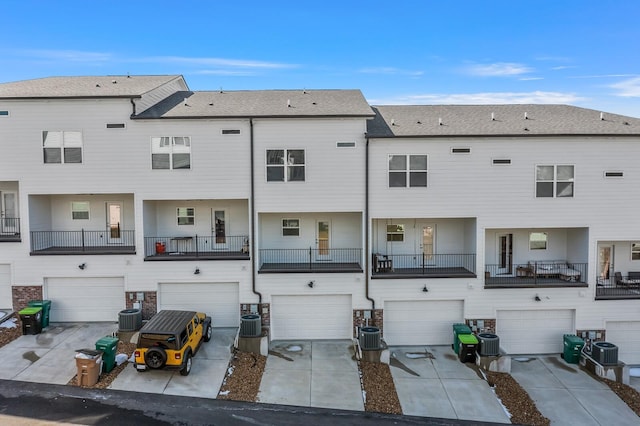 back of property with driveway, stone siding, a garage, and central AC unit