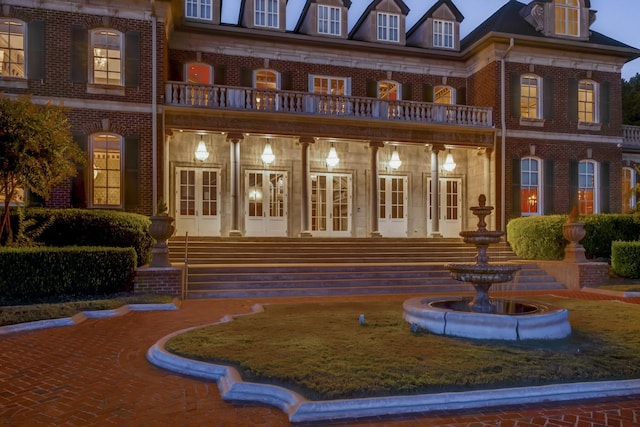 view of exterior entry with french doors, brick siding, and a balcony