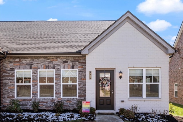 view of exterior entry with stone siding and roof with shingles