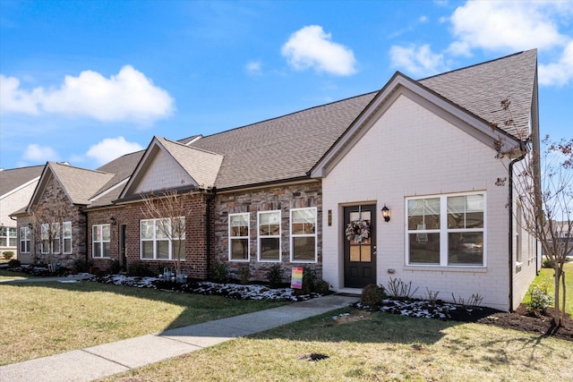 view of front facade featuring a shingled roof, a front yard, and brick siding