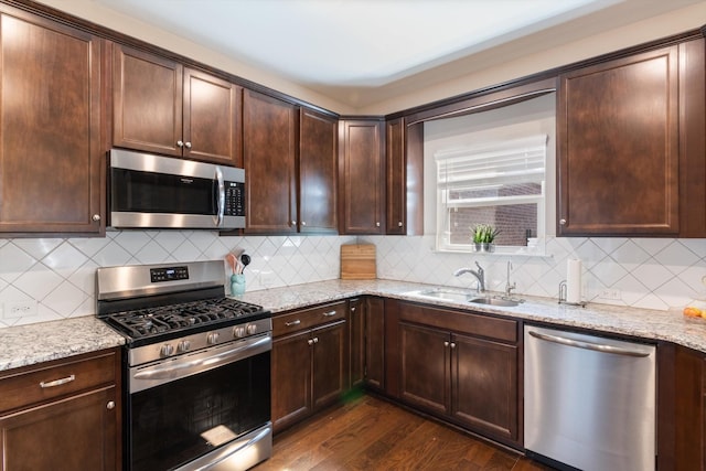 kitchen featuring light stone counters, dark wood-style flooring, appliances with stainless steel finishes, a sink, and dark brown cabinets