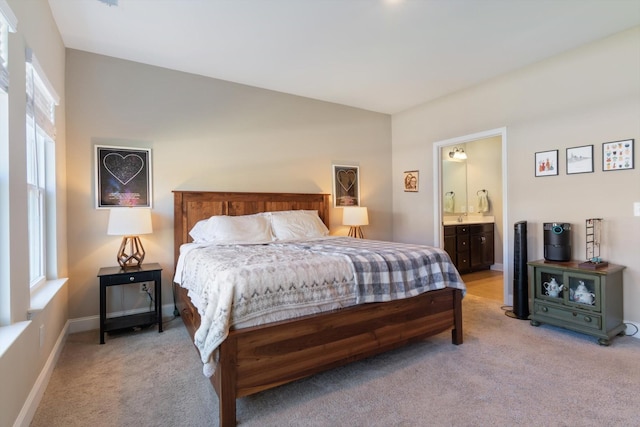 bedroom featuring light carpet, multiple windows, baseboards, and ensuite bathroom