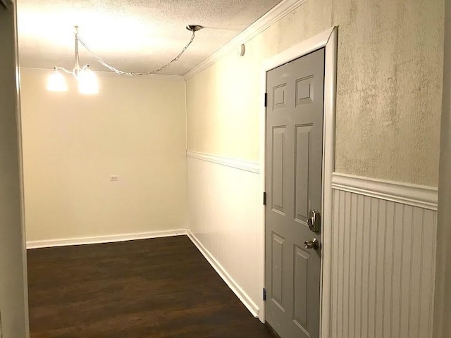 hall featuring a wainscoted wall, dark wood-type flooring, crown molding, a textured ceiling, and a notable chandelier