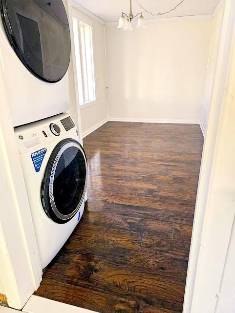 clothes washing area with dark wood-style flooring, a notable chandelier, stacked washer and dryer, laundry area, and baseboards