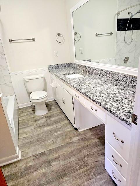 bathroom featuring toilet, tub / shower combination, wood finished floors, and vanity