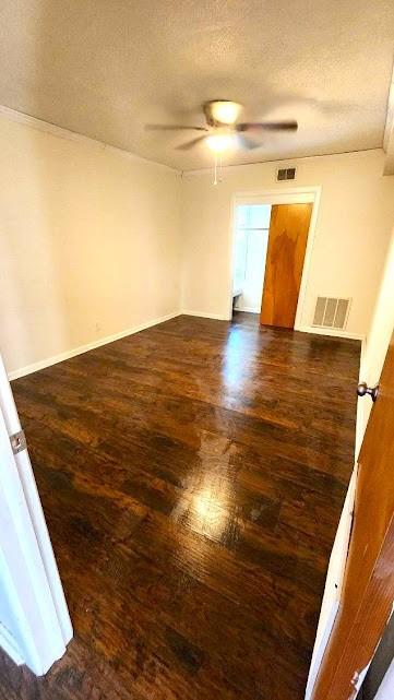 empty room featuring dark wood-style floors, visible vents, a textured ceiling, and a ceiling fan