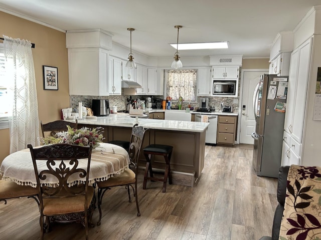 kitchen featuring ornamental molding, under cabinet range hood, appliances with stainless steel finishes, a peninsula, and light countertops