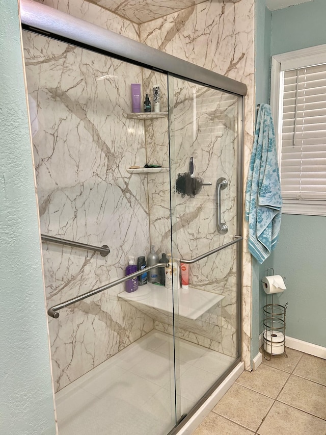 full bath featuring a marble finish shower, tile patterned flooring, and baseboards