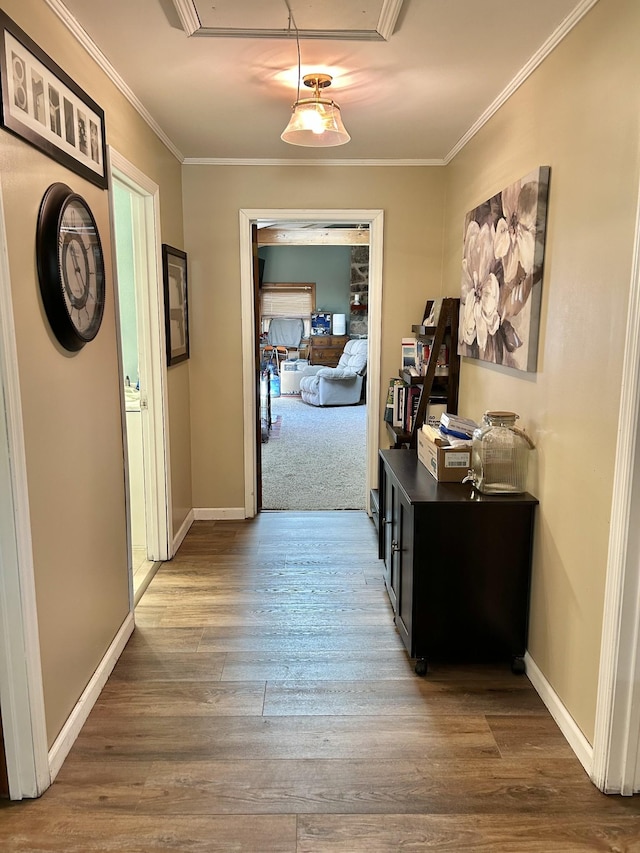 hall with baseboards, wood finished floors, attic access, and ornamental molding