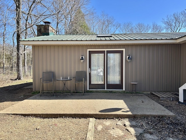 entrance to property featuring a chimney, board and batten siding, metal roof, and fence