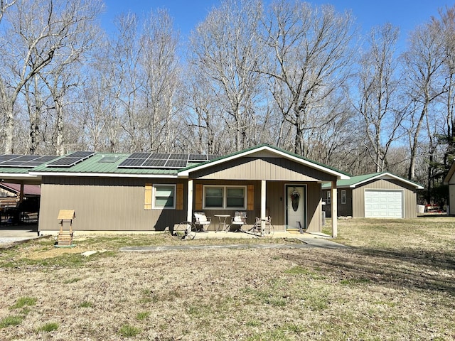 view of front of home with an outbuilding, a detached garage, covered porch, metal roof, and solar panels