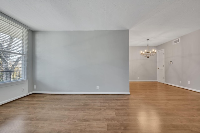 spare room featuring baseboards, visible vents, wood finished floors, a textured ceiling, and a notable chandelier