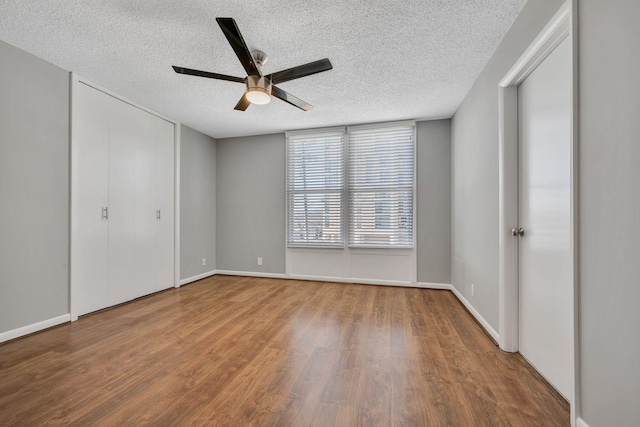 unfurnished bedroom with ceiling fan, a textured ceiling, baseboards, and wood finished floors