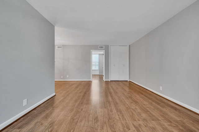 empty room featuring a textured ceiling, light wood-type flooring, visible vents, and baseboards