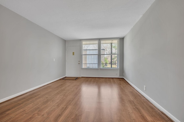 empty room featuring a textured ceiling, wood finished floors, and baseboards