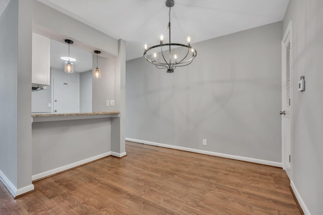 unfurnished dining area with a notable chandelier, baseboards, and wood finished floors