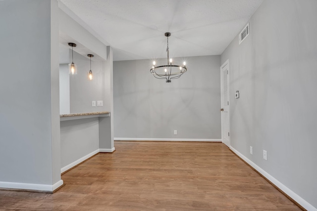 unfurnished dining area featuring a chandelier, light wood finished floors, visible vents, and baseboards