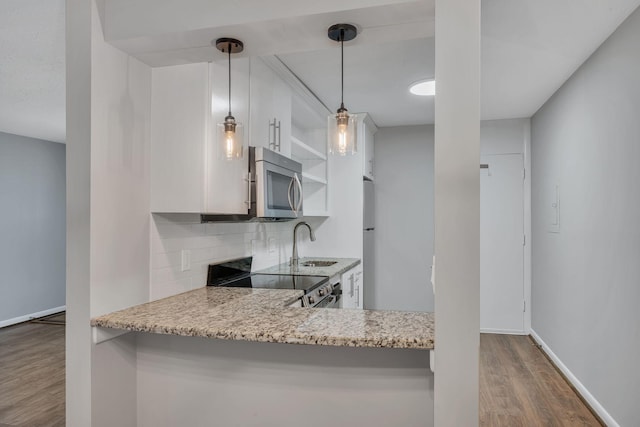 kitchen featuring pendant lighting, backsplash, appliances with stainless steel finishes, a sink, and wood finished floors