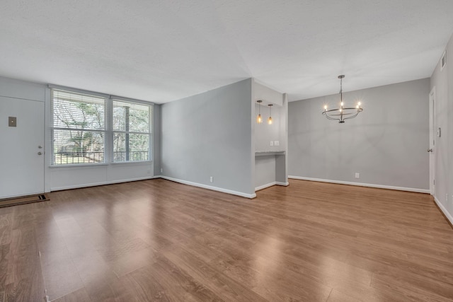 unfurnished living room with a textured ceiling, baseboards, wood finished floors, and an inviting chandelier