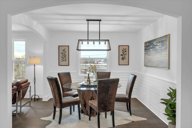 dining room with arched walkways, dark wood-style flooring, and a wainscoted wall