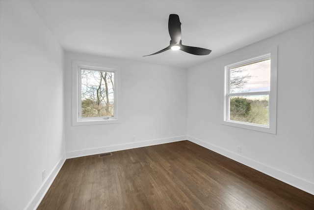 empty room with baseboards, dark wood-type flooring, visible vents, and a healthy amount of sunlight