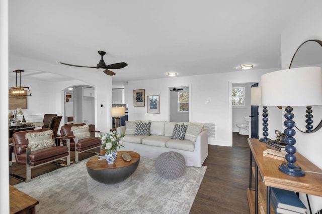 living area featuring baseboards, arched walkways, dark wood finished floors, and a ceiling fan