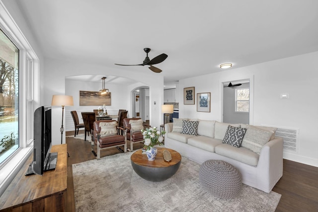 living room featuring arched walkways, ceiling fan, dark wood-type flooring, visible vents, and baseboards