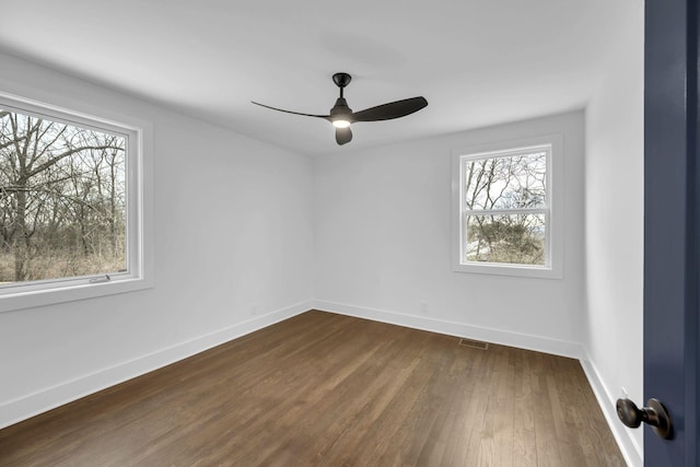 unfurnished room with visible vents, dark wood finished floors, a ceiling fan, and baseboards